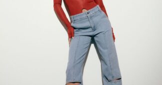 LSU gymnast Livvy Dunne is posing for a photograph while wearing a red, long-sleeved top and faded, high-waisted blue jeans.