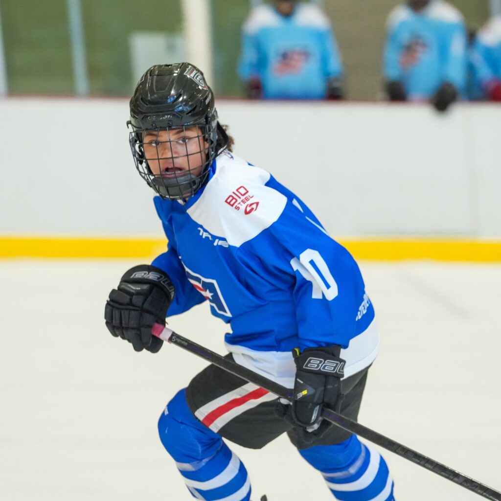 Chloe Brinson is pictured in a blue and white hockey jersey, skating on the ice while participating in the BioSteel Player Development Girls 15 camp.