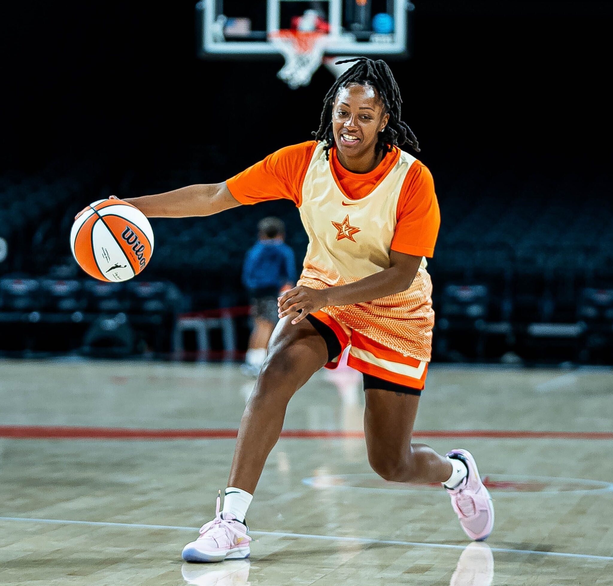 Indiana Fever guard Kelsey Mitchell, wearing orange All-Star gear, handles the ball with her right hand in All-Star practice.