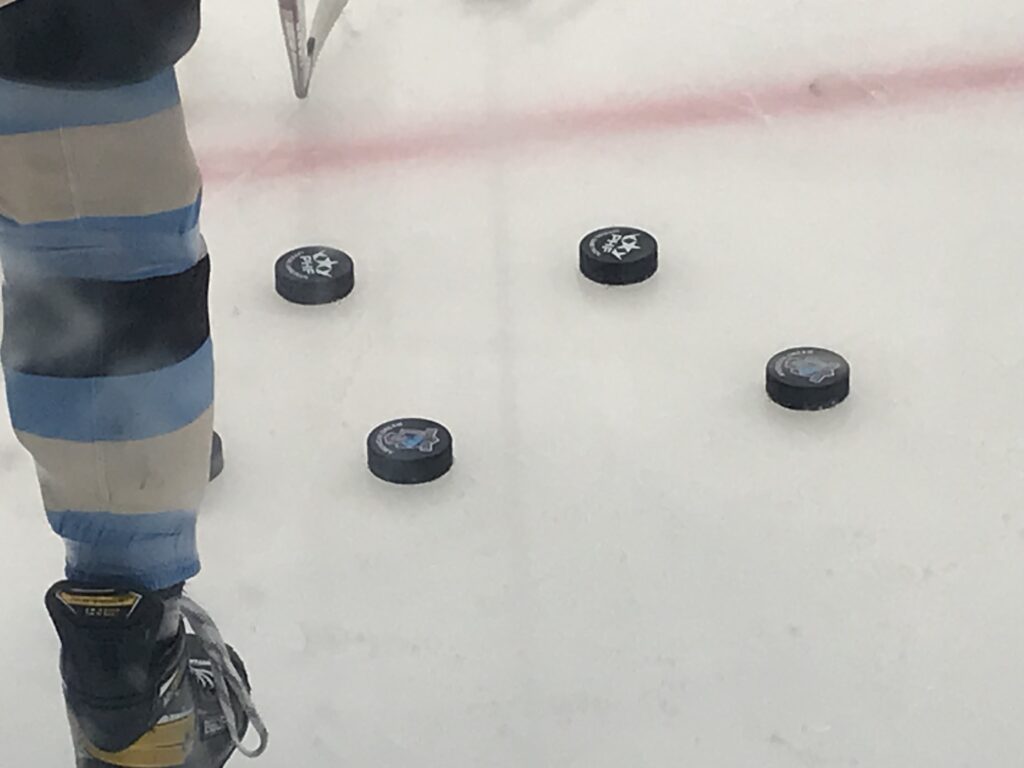 A player's hockey skate is pictured next two four hockey pucks on the ice.
