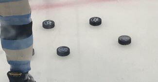 A player's hockey skate is pictured next two four hockey pucks on the ice.