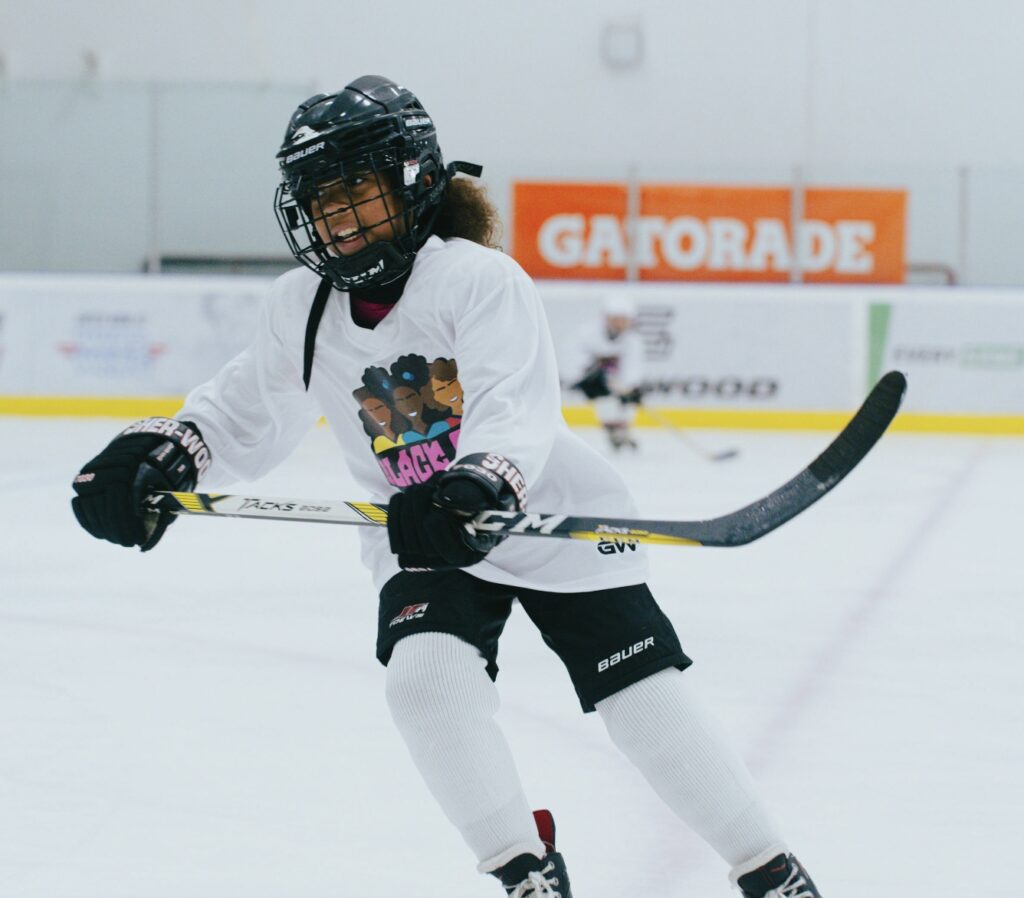 A child hockey player skates across the ice wearing a white jersey with the Black Girl Hockey Club logo.