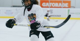 A child hockey player skates across the ice wearing a white jersey with the Black Girl Hockey Club logo.