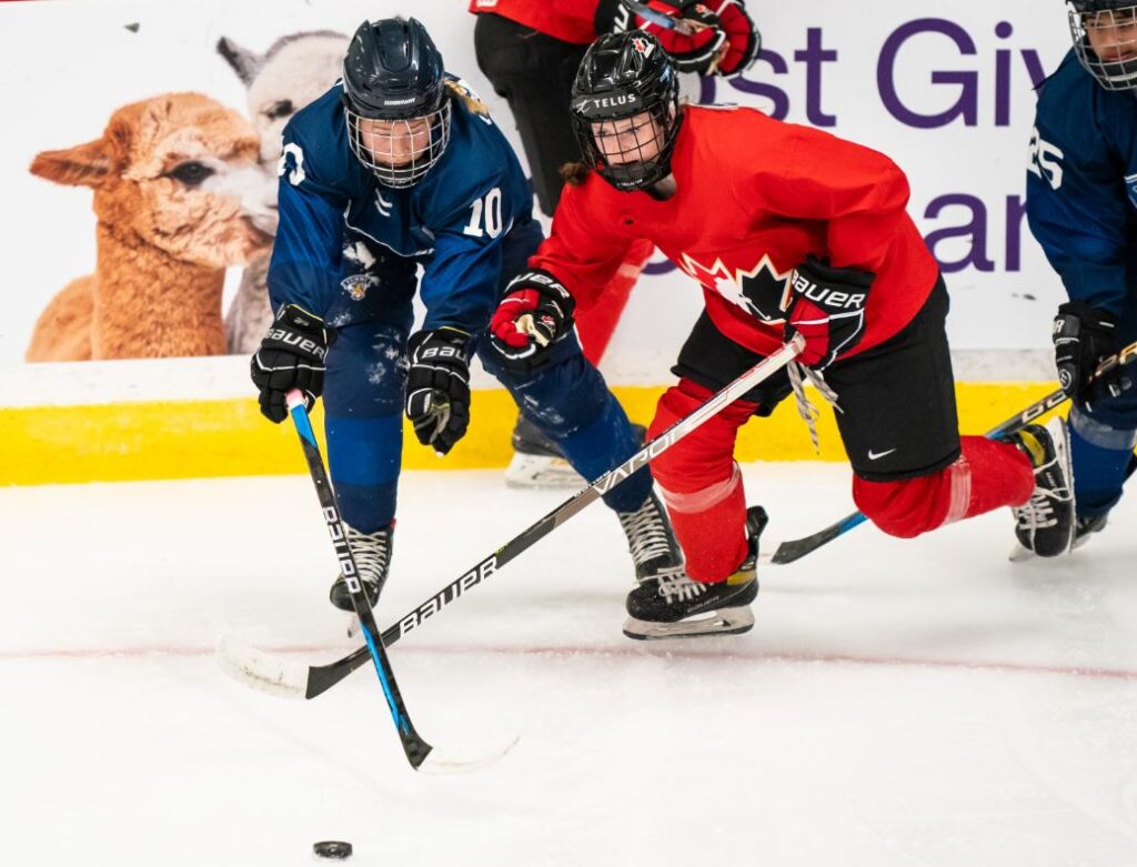 Sienna D’Alessandro wearing a red Team Canada jersey fights on the ice for position to get the puck against an opposing player in a blue jersey during Team Canada's U18 Selection Camp.