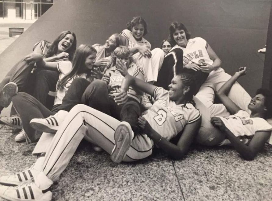 A black and white photograph of the WBL team Chicago Hustle shows the players piled on the floor smiling and laughing.