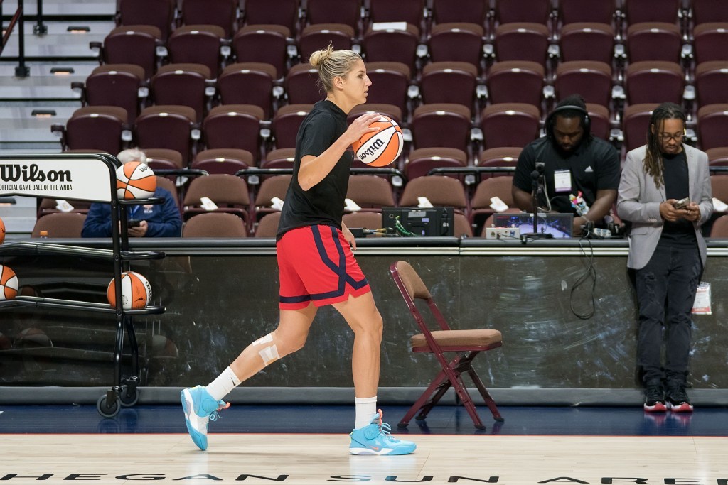 Washington Mystics forward Elena Delle Donne dribbles a ball with her right hand near the sidelines during warmups. She is wearing a black shirt and red shorts and has tape on her left shin.