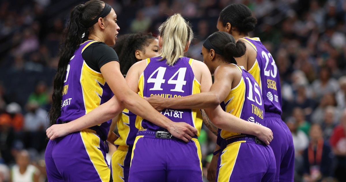 Five Los Angeles Sparks players wrap their arms around each other's waists as they huddle.