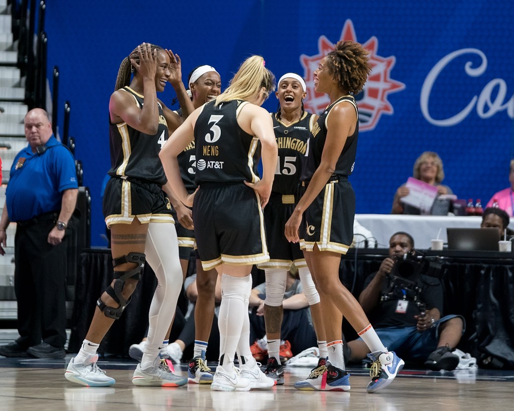 Five Washington Mystics players smile and laugh in a huddle.