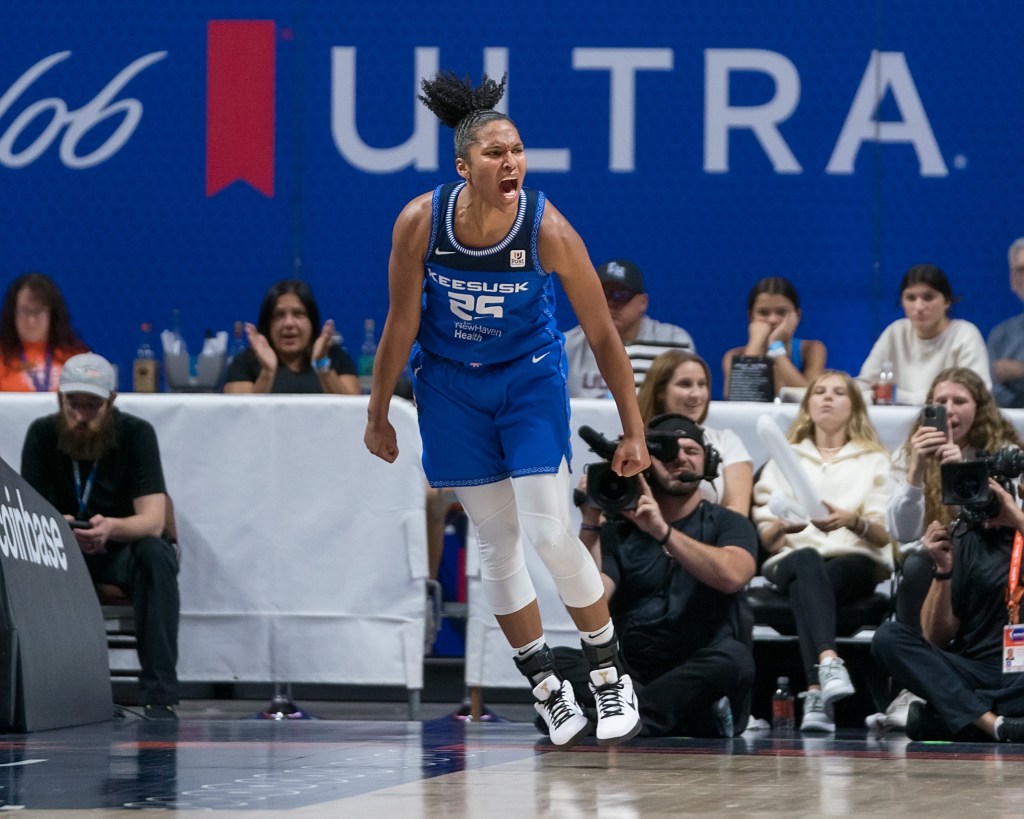 In mid-air, Connecticut Sun forward Alyssa Thomas looks to her left and shouts in celebration.