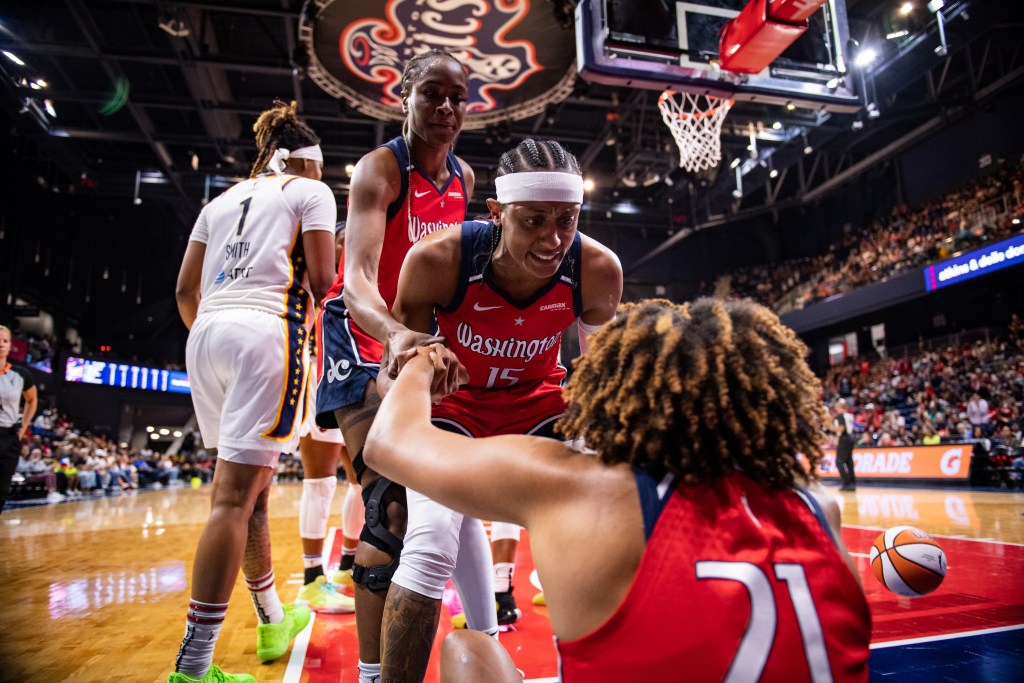 Washington Mystics guard Brittney Sykes pulls up forward Tianna Hawkins, who had fallen to the floor. Center Queen Egbo also extends an arm to assist.