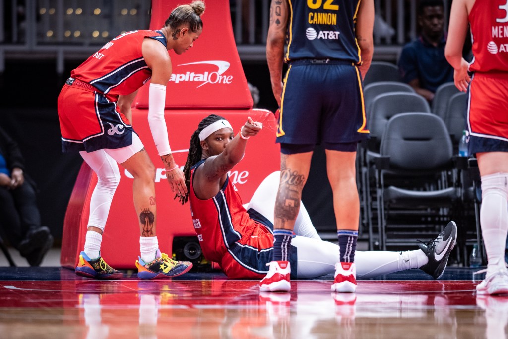 Washington Mystics forward Myisha Hines-Allen sits on the baseline and stares and points in celebration after making a play. Guard Natasha Cloud comes from behind her to help her up.