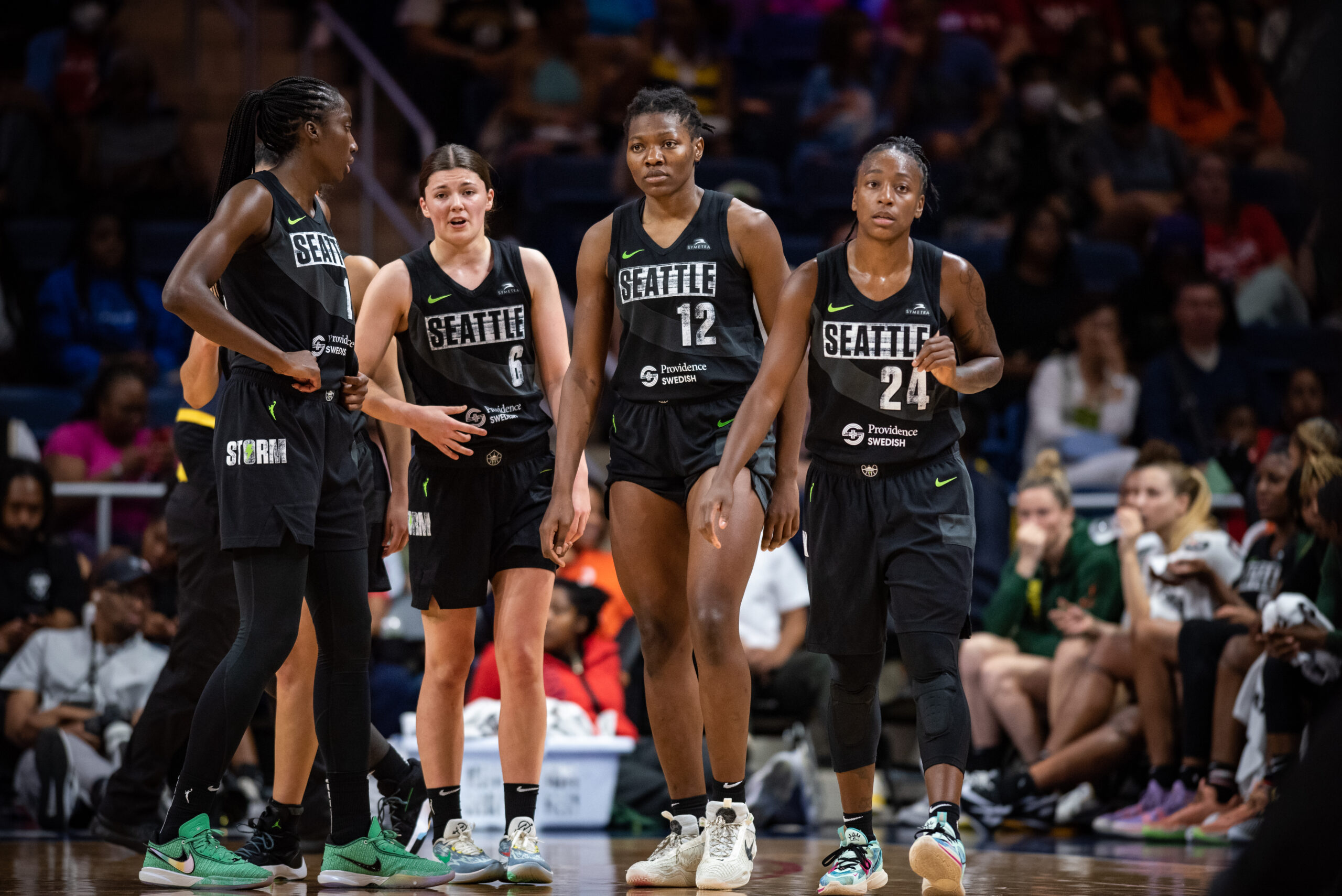 Wearing all-black uniforms, four Seattle Storm players walk onto the court together.