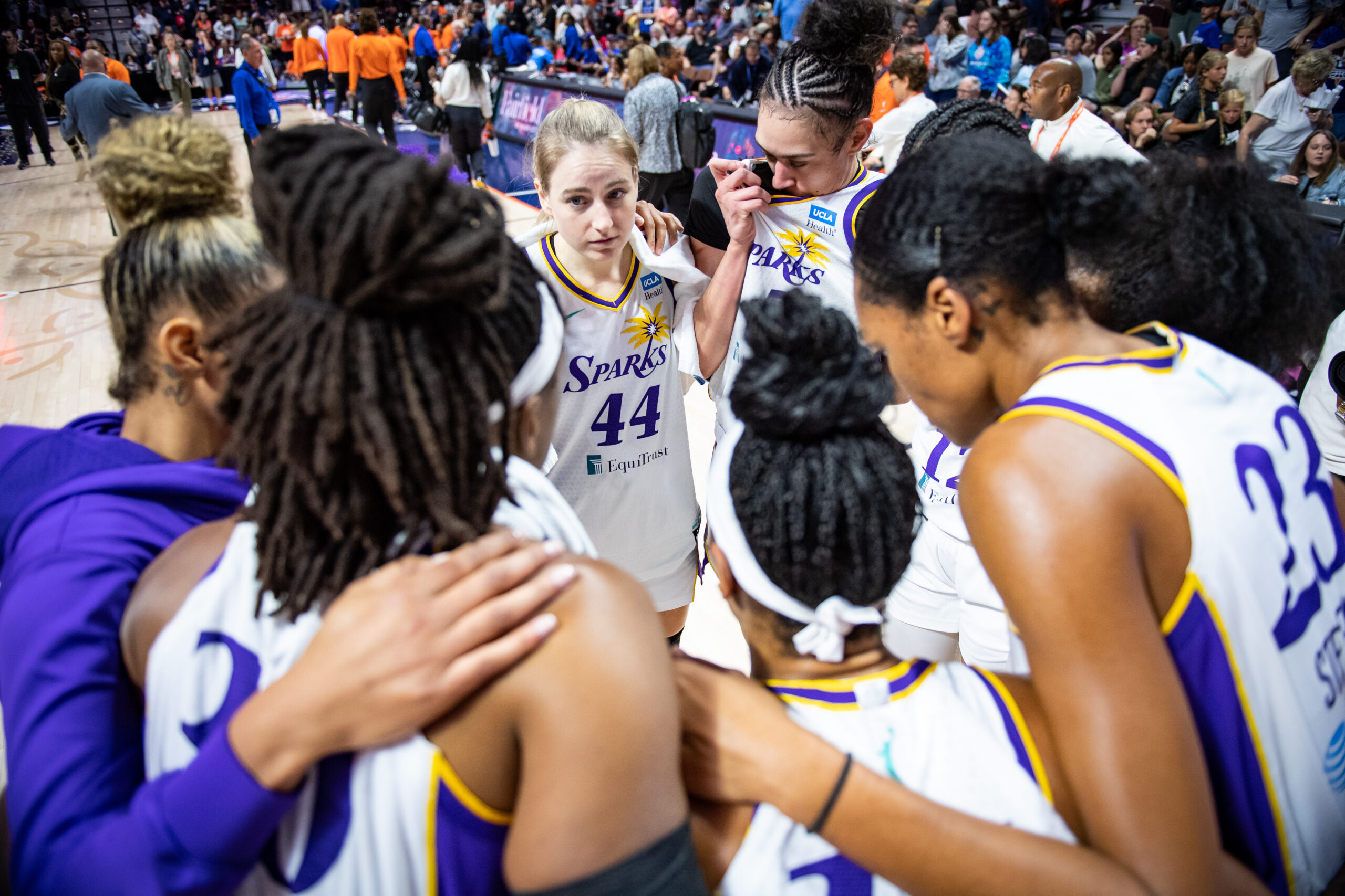 Members of the Los Angeles Sparks huddle together. They are wearing their team uniforms.
