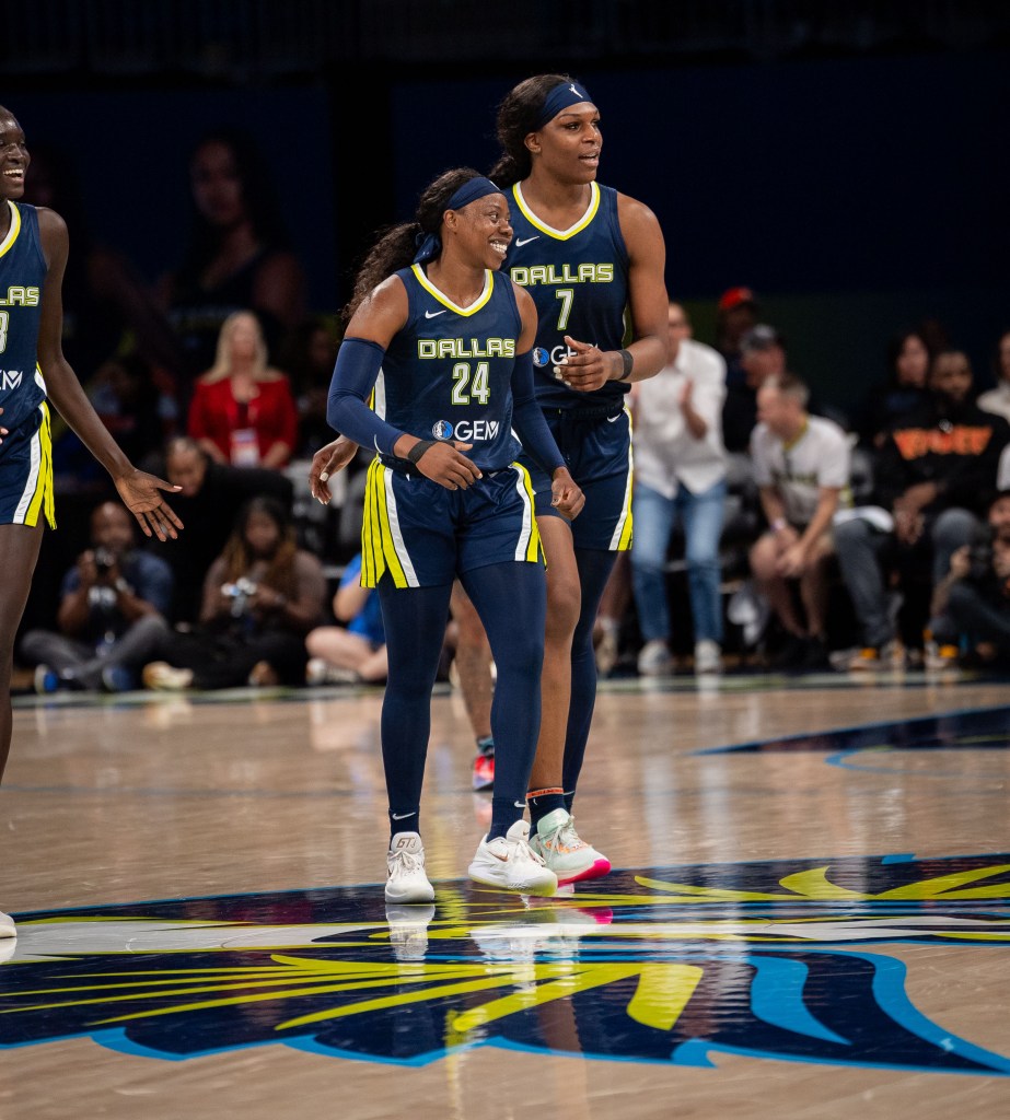 Dallas Wings guard Arike Ogunbowale and center Teaira McCowan smile as they stand on the Wings logo at half court.