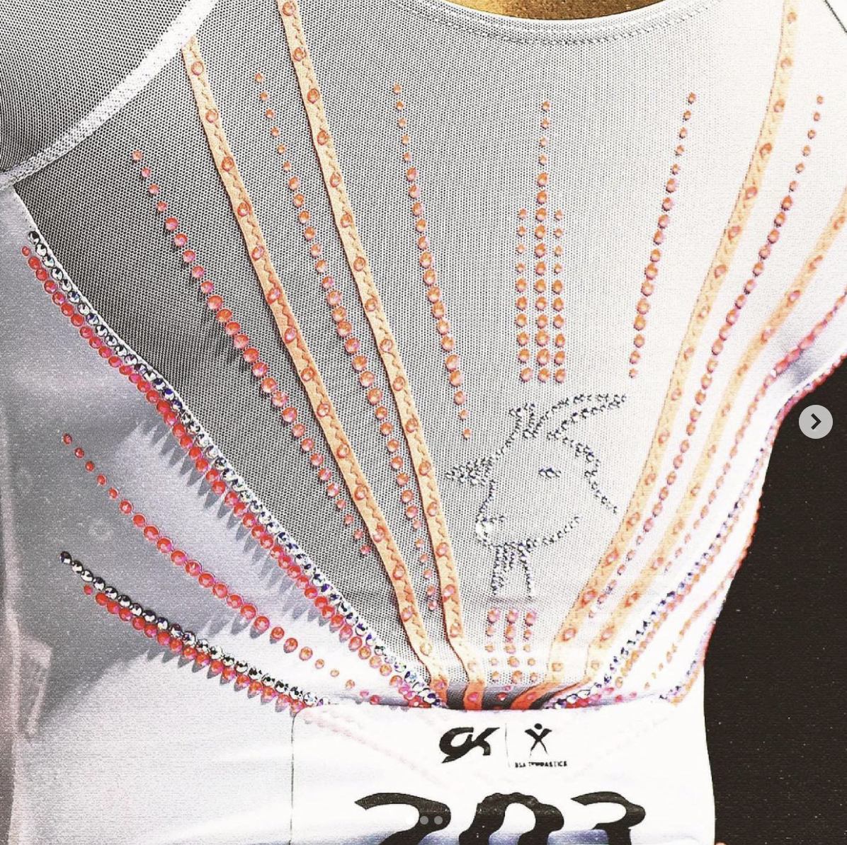 A close-up shot of a white Simone Biles leotard with pink and orange rhinestones and a silver rhinestone goat silhouette.