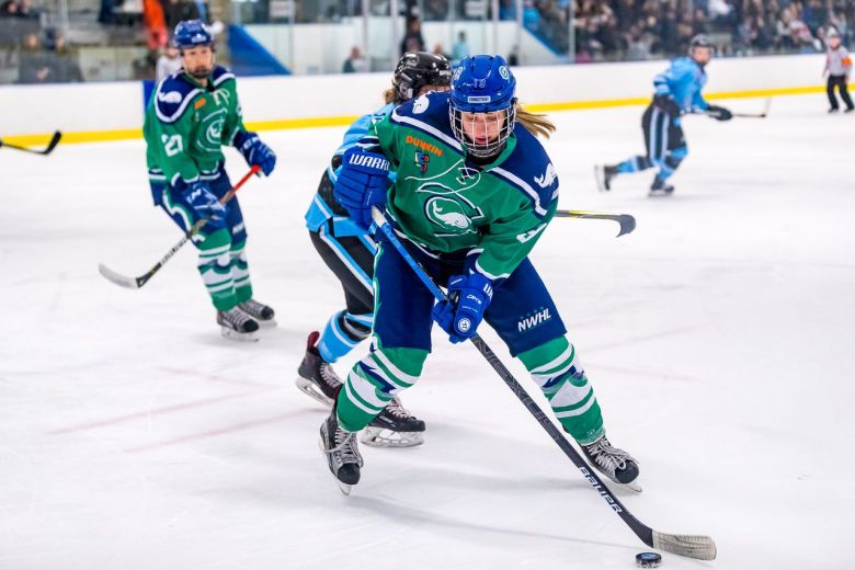 Janine Weber handles the puck while wearing green Whale uniform.