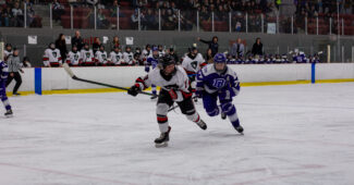 A Carleton University hockey player and Bishop's University player chase a puck.