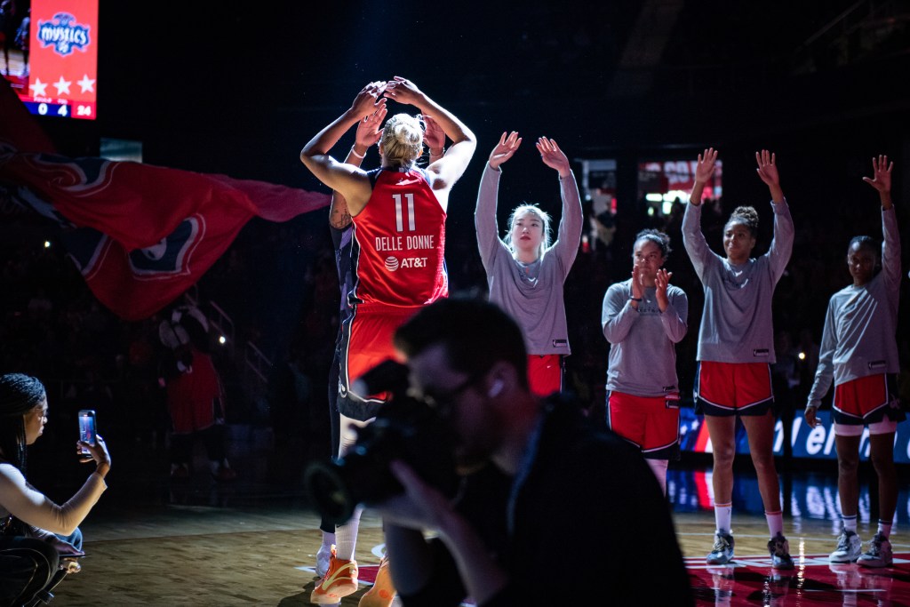 Washington Mystics forward Elena Delle Donne approaches her teammates, who are wearing warmup shirts and standing in a line, for high-fives before a game.