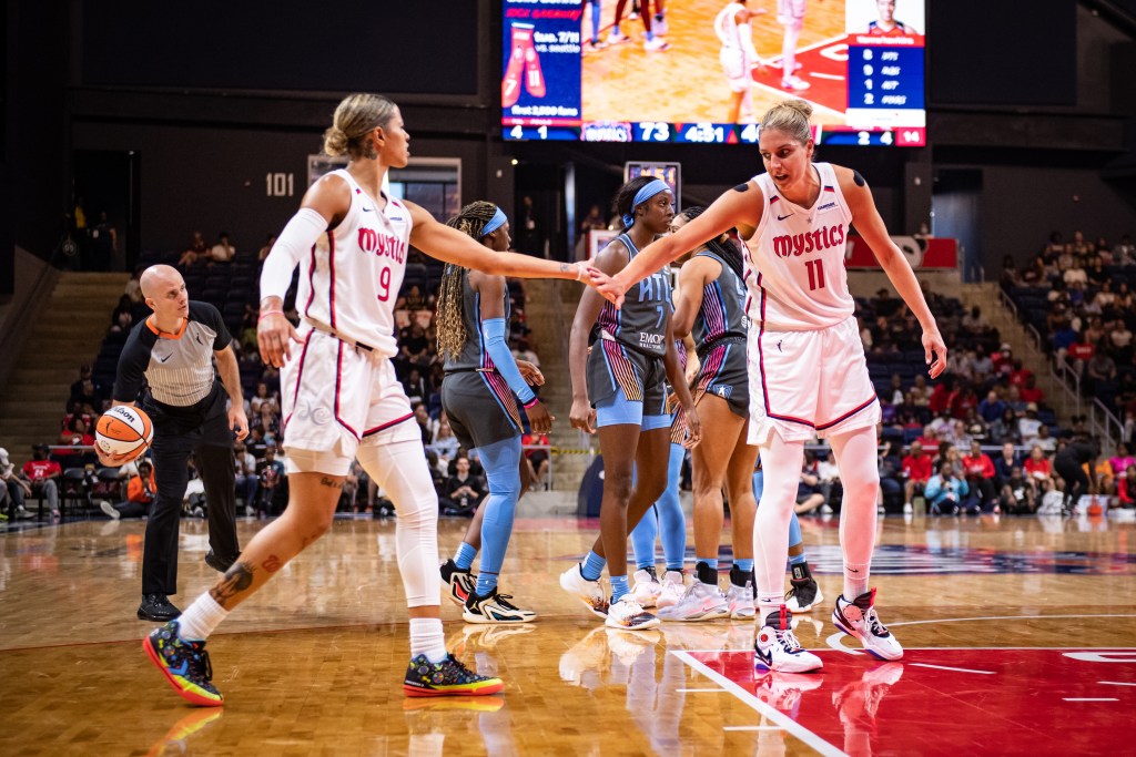 Washington Mystics guard Natasha Cloud walks toward forward Elena Delle Donne with her left arm extended. Delle Donne reaches out with her right arm to high-five Cloud.