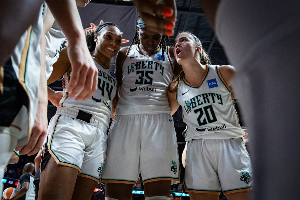 Betnijah Laney, Jonquel Jones and Sabrina Ionescu participate in a New York Liberty huddle.  They are pictured wearing white Liberty jerseys.