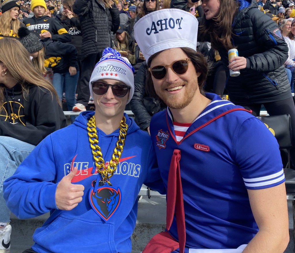 DePaul fans Ethan Brock and Tim Anderson are decked out in Blue Demons gear. Brock wears a thick gold chain with a Blue Demons logo, while Anderson has on a sailor hat and top with the DePaul logo.