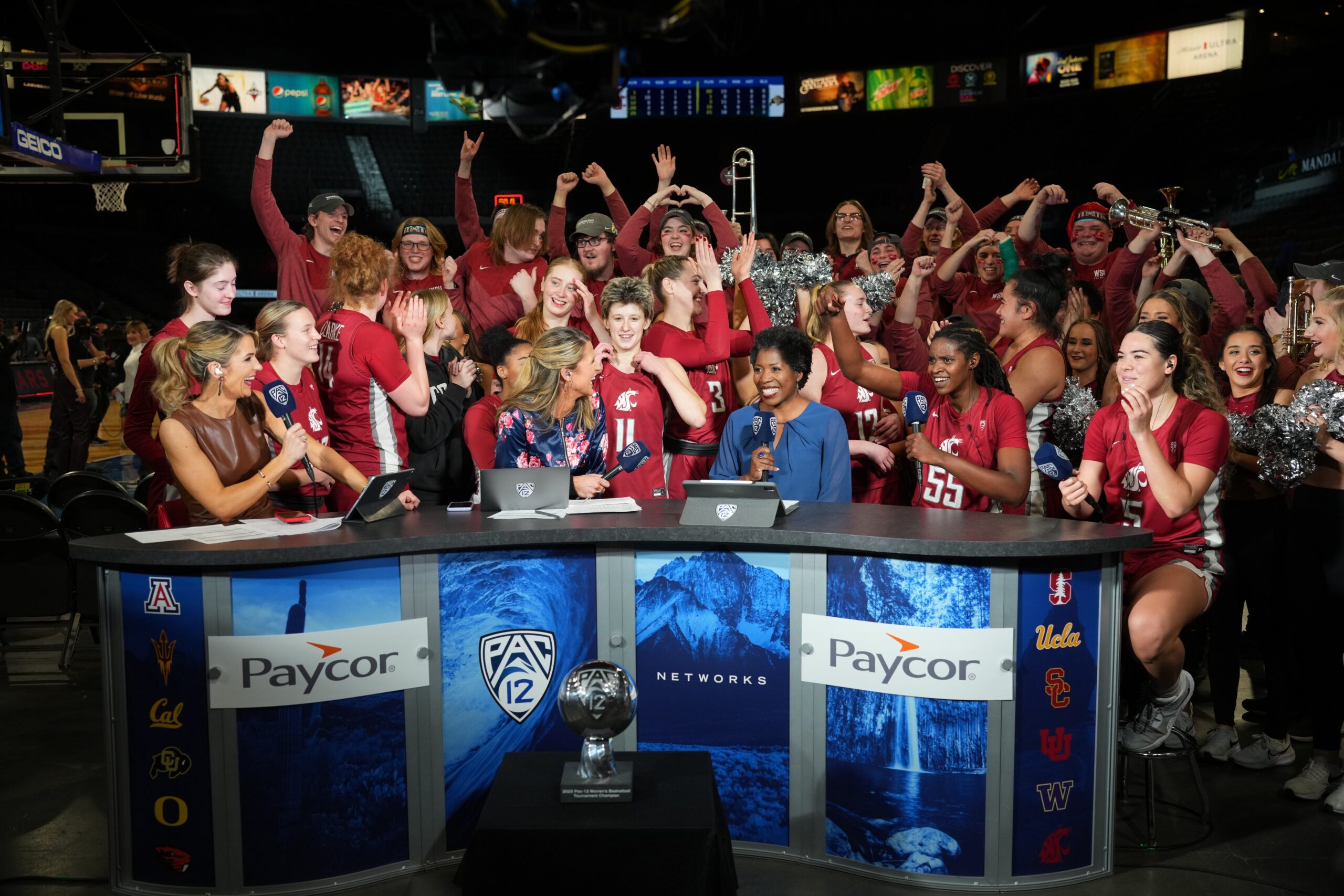 Washington State players surround the Pac-12 broadcasting desk in celebration after winning their first Pac-12 championship.