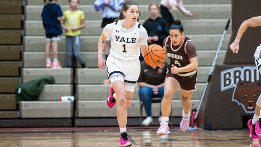 Yale point guard Jenna Clark dribbles the ball with her left hand in transition, looking downcourt. Trailing the play, Brown guard Isabella Mauricio has her eyes on Clark.