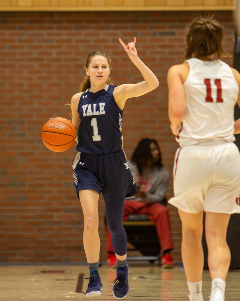 Yale point guard Jenna Clark dribbles the ball with her right hand and holds her left hand high to signal a play.