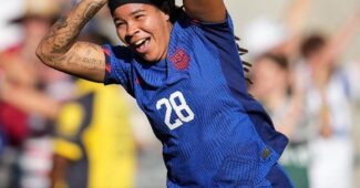 USWNT forward celebrates a goal Mia Fishel celebrates a goal during a game against Colombia. She is mimicking fish fins while running across the field in a blue #28 USWNT jersey.