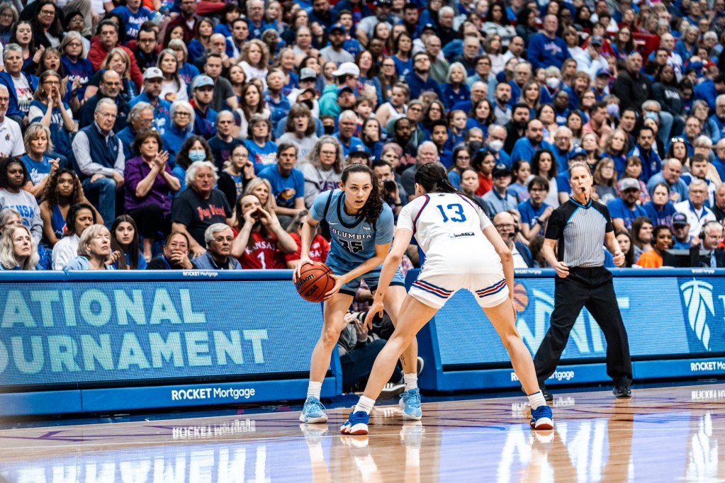 Columbia guard Abbey Hsu holds the ball with both hands near her right hip. She stands on the perimeter with a defender squared up to her and scans the court.