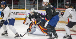 Three players screen a goalie crouching to make a save.