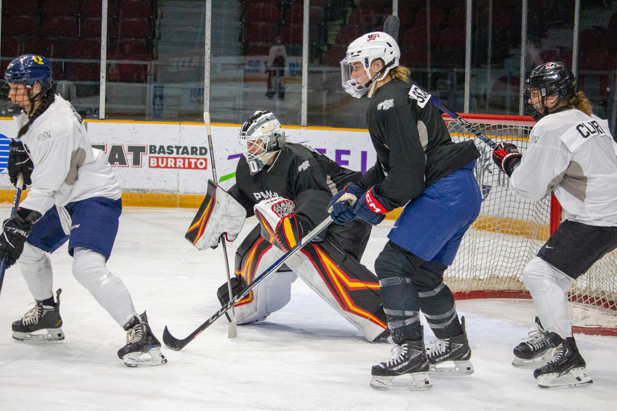 Three players screen a goalie crouching to make a save.