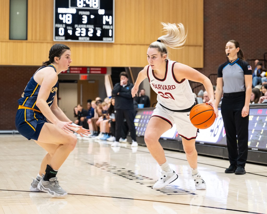 Harvard guard Lola Mullaney dribbles the ball with her left hand just outside the 3-point line. A defender slides her feet to try to stay with Mullaney.