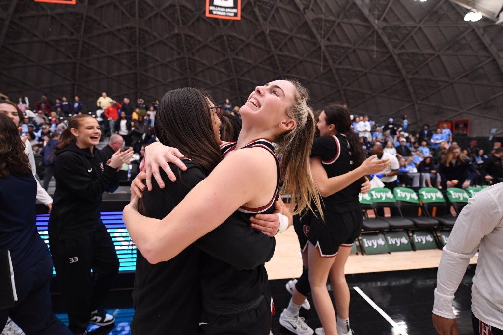 Harvard guard Lola Mullaney and head coach Carrie Moore embrace after a win. Mullaney is beaming, her head tilted toward the sky.