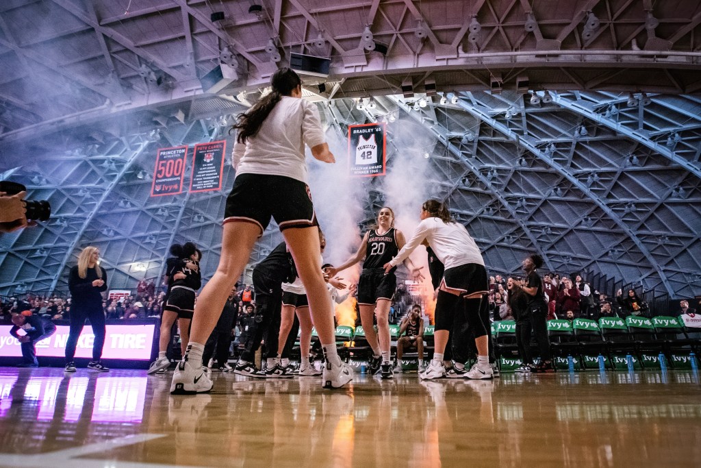 Harvard guard Lola Mullaney smiles and high-fives her teammates as she is introduced in the starting lineup. Smoke is shot out of two cannons behind her.