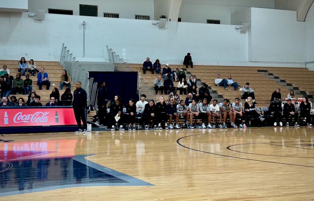 Georgetown graduate assistant Bella Alarie sits on the bench and looks toward the far end of the court, where the game action is happening.