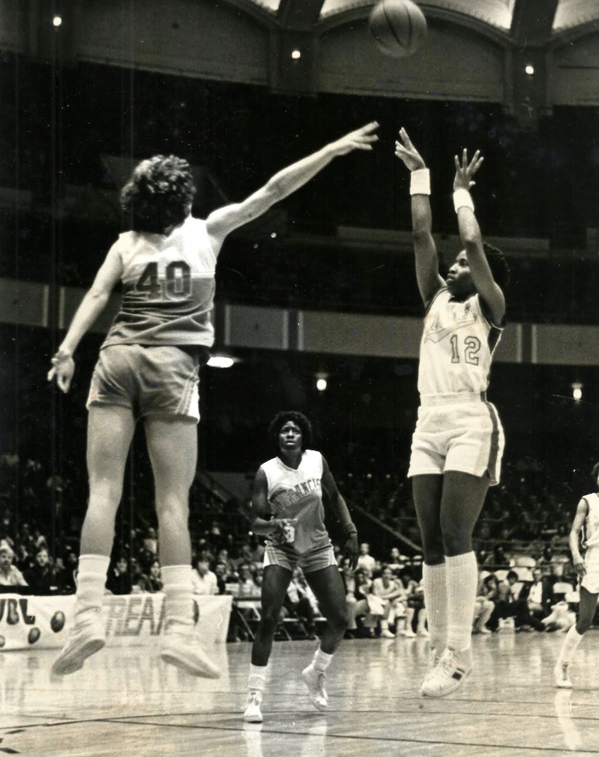 WBL legend Pearl Moore is pictured in a black and white photo shooting a jump shot over a defender.