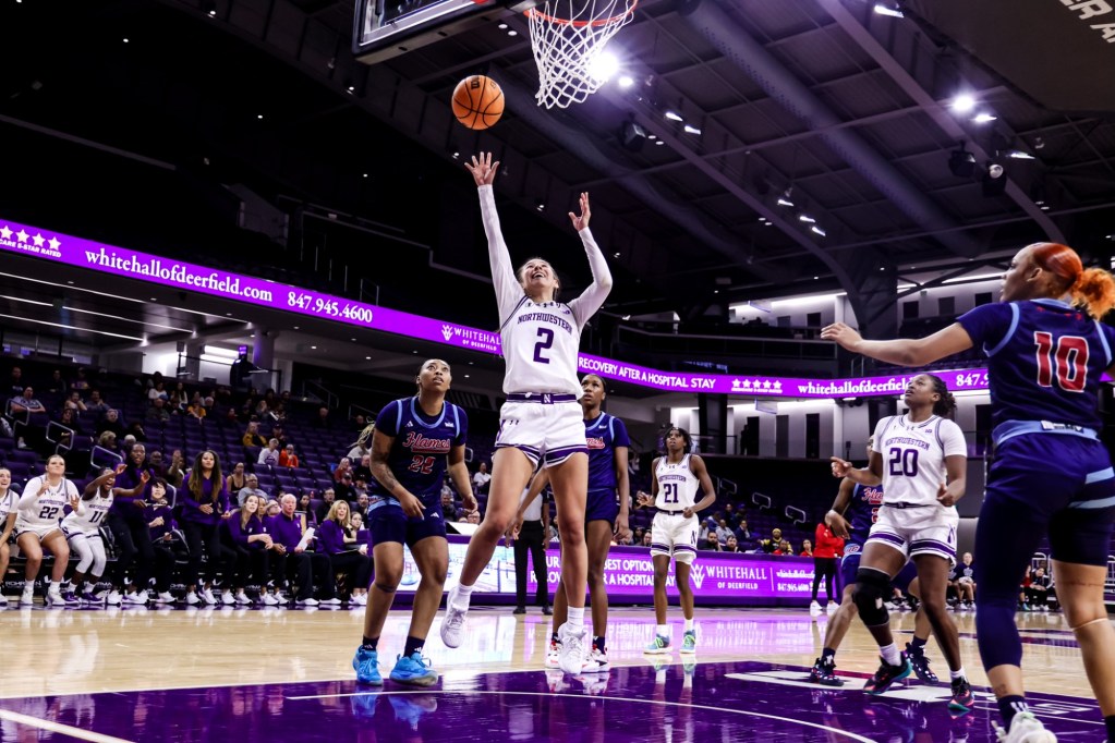 Northwestern guard Caroline Lau (2) goes for a layup just under the basket during a game against UIC. Other players from both teams surround the paint as Lau extends her right arm for the shot.