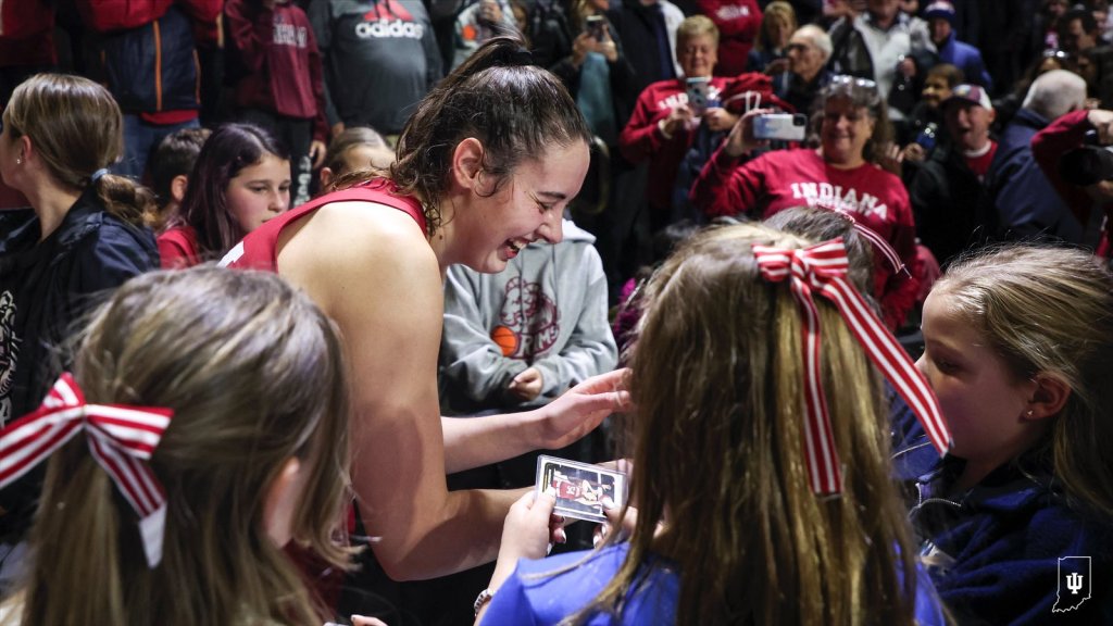 Mackenzie Holmes signs basketball cards while surrounded by young fans with Indiana red-and-white bows in their hair.