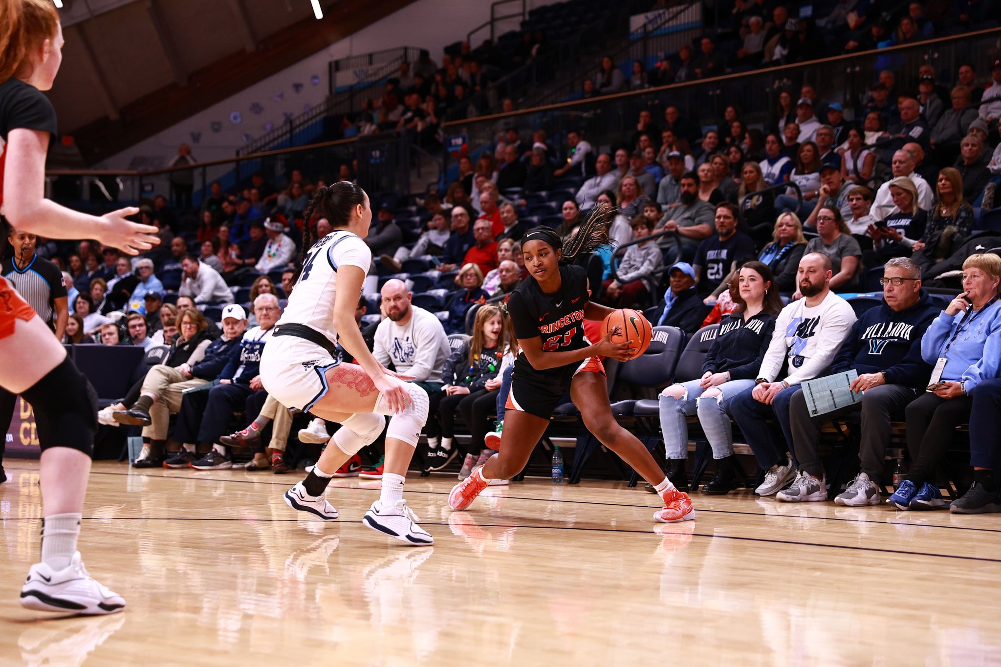 Princeton sophomore guard Madison St. Rose in a black princeton jersey with orange lettering and numbers faces up towards the camera with the ball against a Villanova defender in a white jersey, perpendicular to the camera.