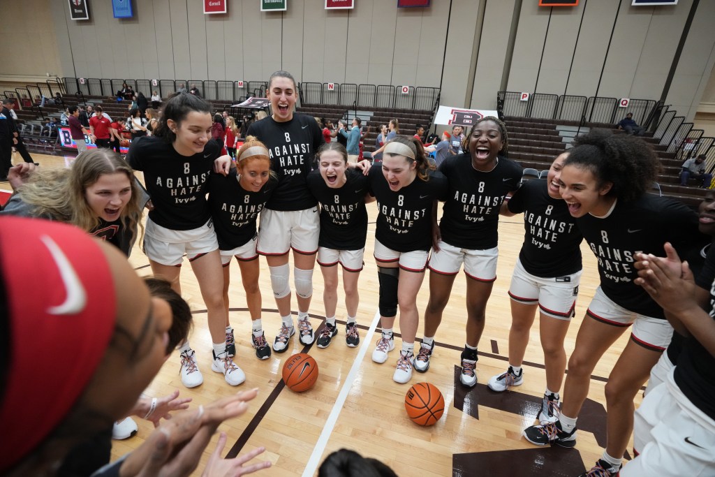 Brown players are shown in a huddle, smiling and shouting with their arms wrapped around each other.