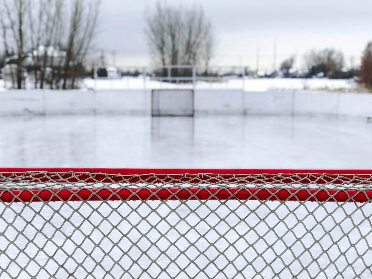 The view from behind a hockey net of an outdoor hockey rink.