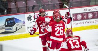 Boston University players, wearing red home uniforms, celebrate a goal against Boston College.