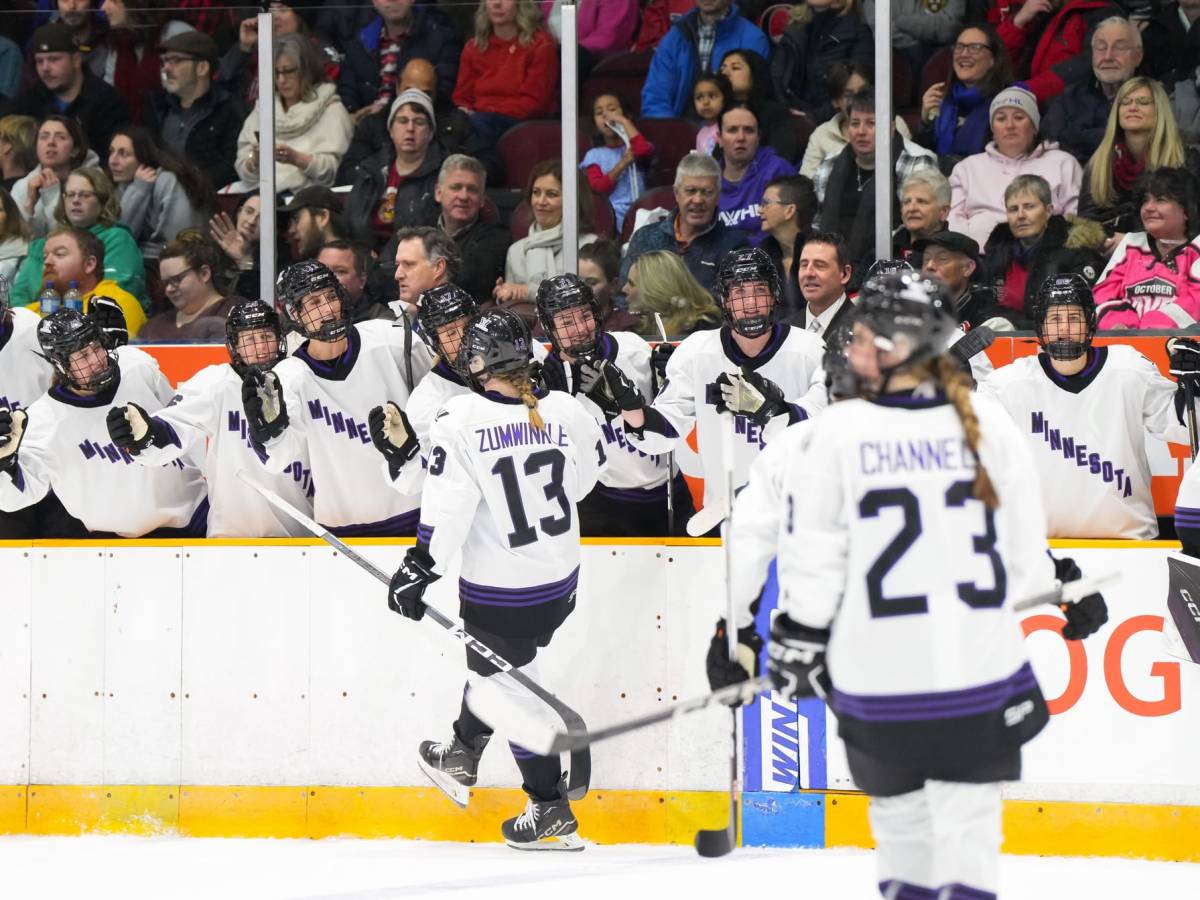 Grace Zumwinkle and her teammates, wearing their white away uniforms, celebrate her goal at the bench.