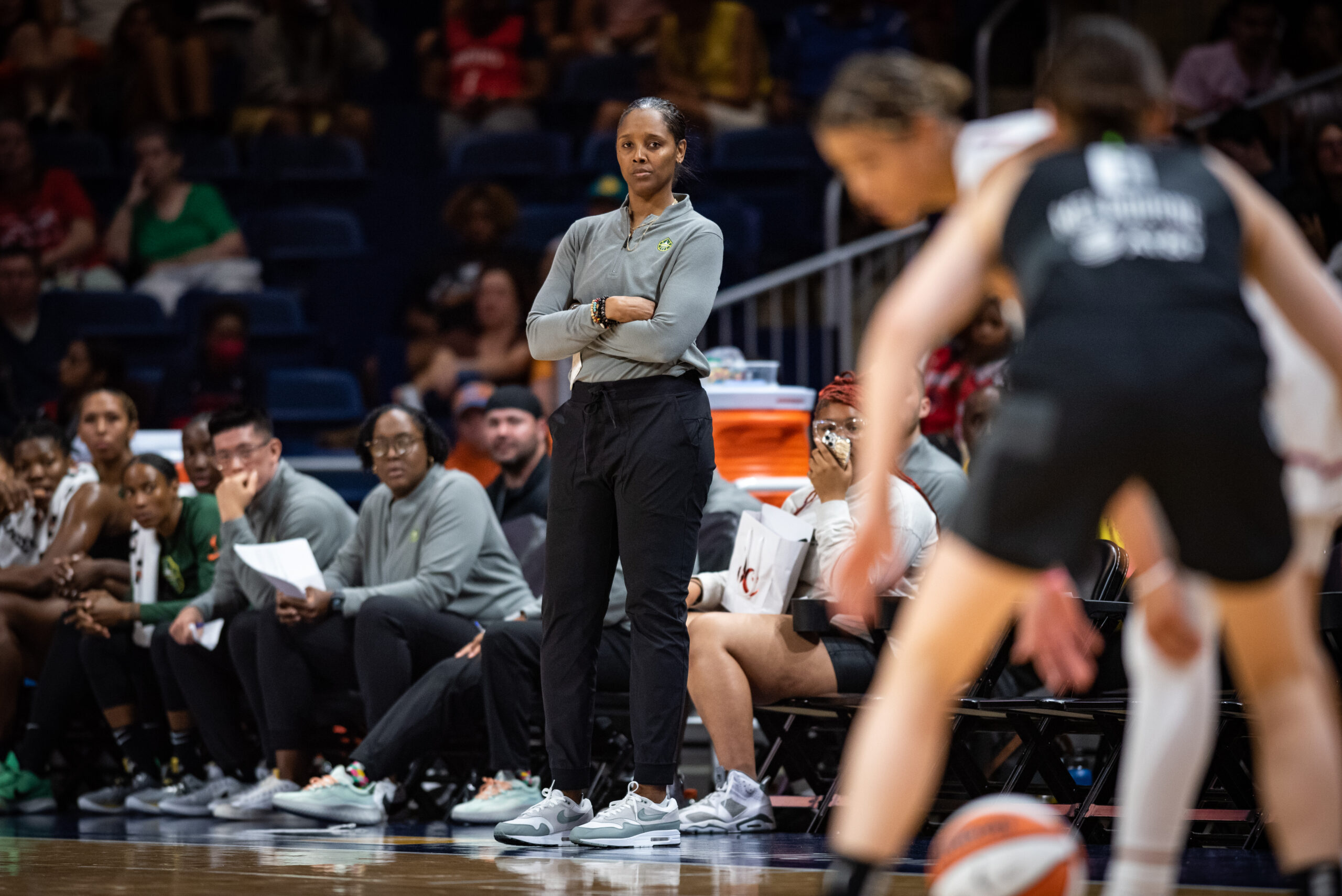 Seattle Storm head coach Noelle Quinn stands on the sidelines and watches her team play with her arms folded across her chest.