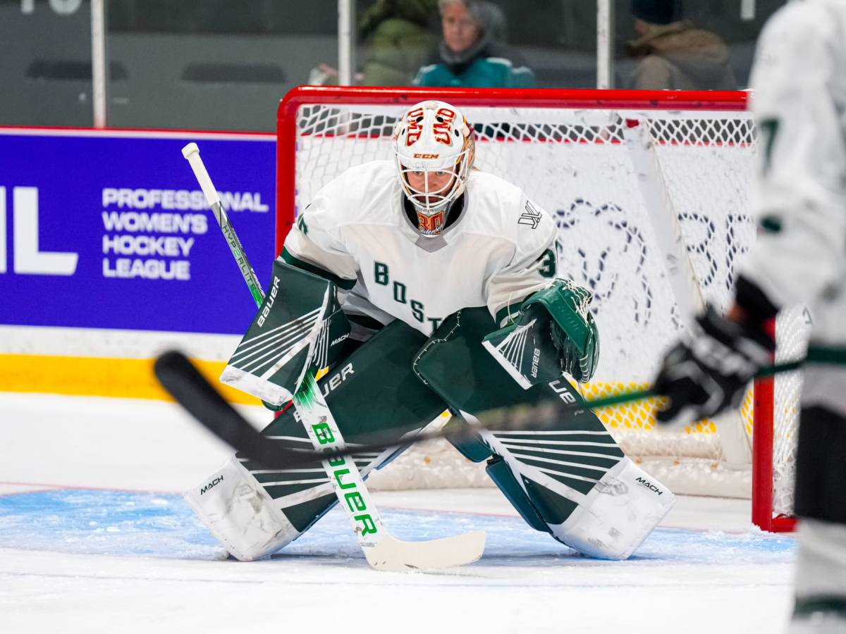 Emma Söderberg, wearing a white jersey, green pads, and a UMD mask, prepares to make a save during warm-ups of a prior game.