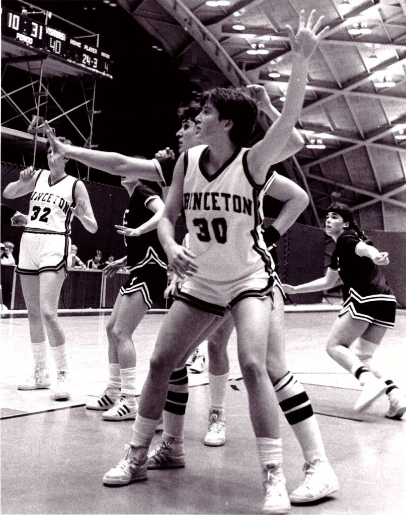 In a black-and-white photo, Princeton forward Ellen DeVoe stands in the lane facing the basket and uses her left hand to show where a teammate can pass her the ball.