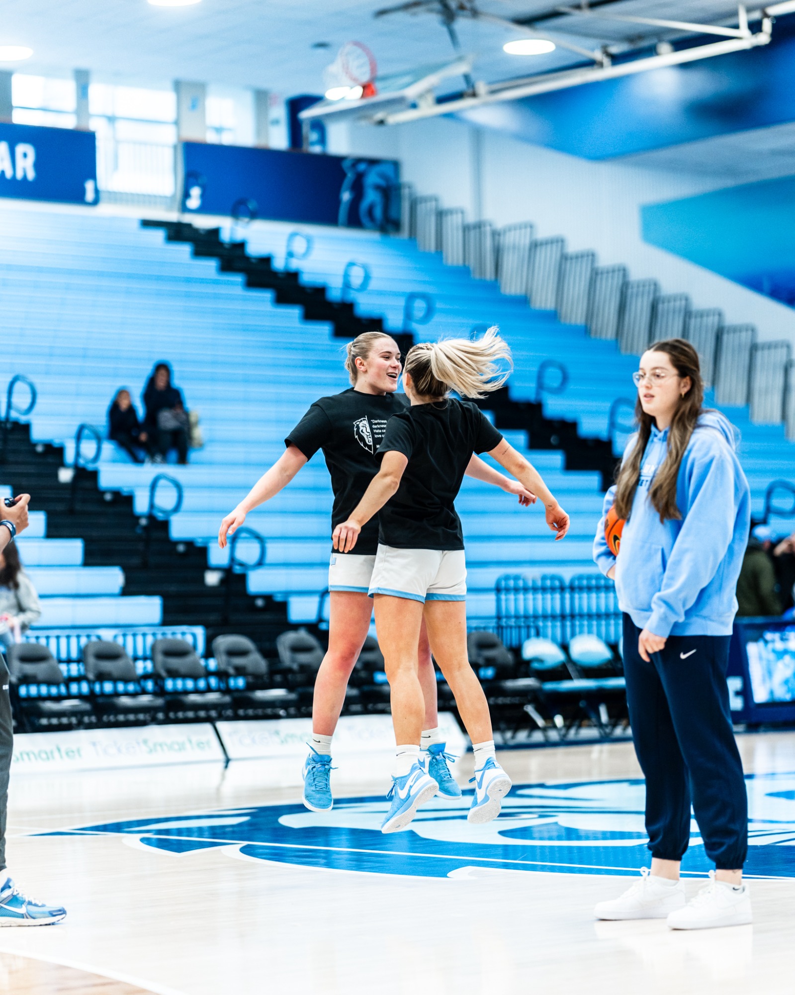 Near center court, Columbia guards Fliss and Kitty Henderson jump in the air facing each other and bump chests.