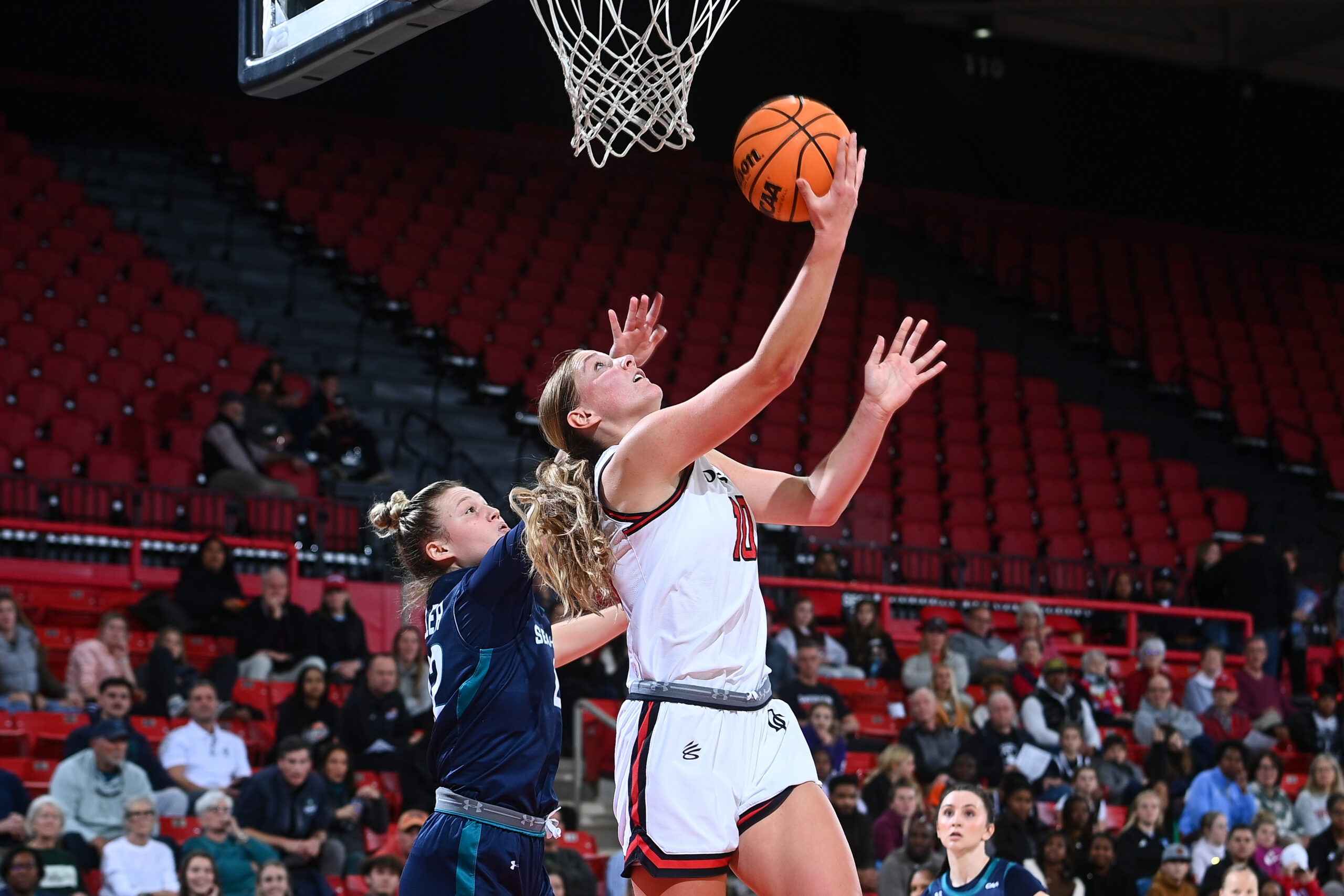 Millie Prior goes up around the defender for a reverse layup. She is looking up at the basket about the release the ball with her right hand.