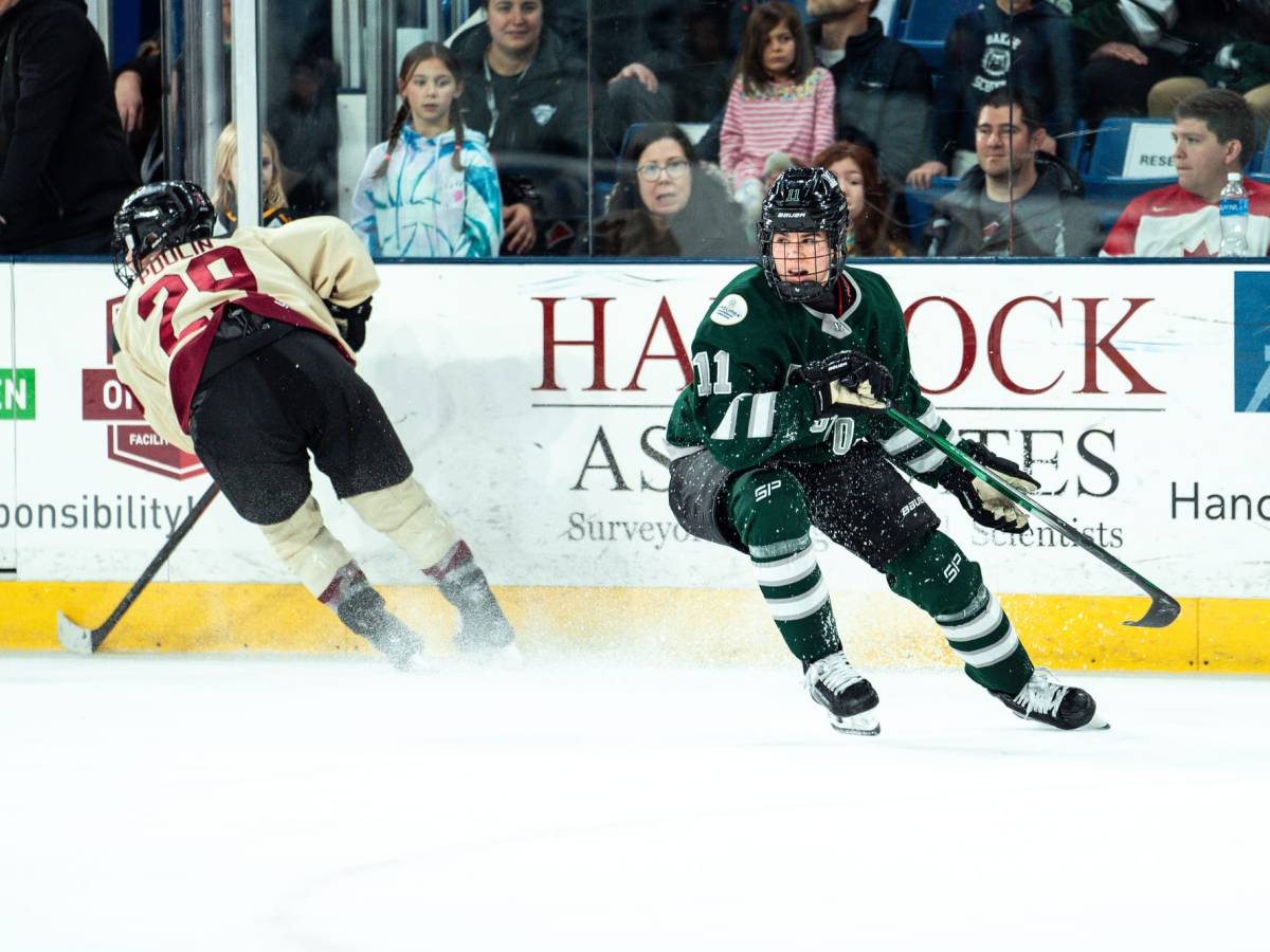 Alina Müller, wearing a green home uniform, and Marie-Philip Poulin, wearing a cream away uniform, turn towards a play.